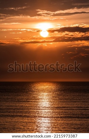 A mysterious-looking sunset with a reddish light and some dark clouds around the sun on wadden sea island Texel in the Netherlands Royalty-Free Stock Photo #2215973387