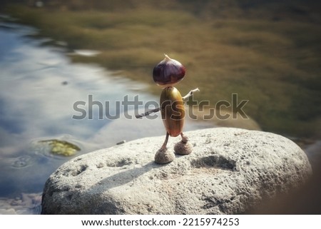 a toy acorn man stands on a stone in a forest stream
