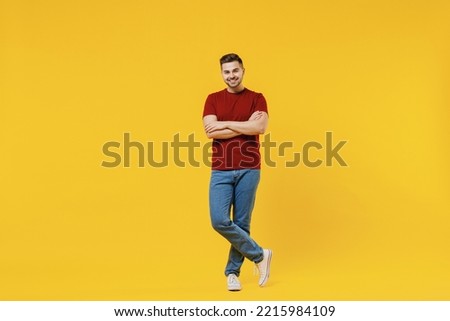 Full length smiling caucasian happy young man 20s wear red t-shirt casual clothes holding hands crossed folded isolated on plain yellow color wall background studio portrait. People lifestyle concept