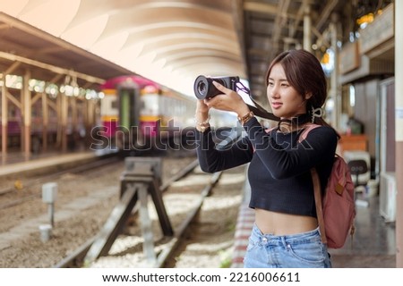 woman wearing black long sleeve t-shirt carrying backpack on shouder holding digial camera in hands standing in railway station,travel concept,social network technology concept