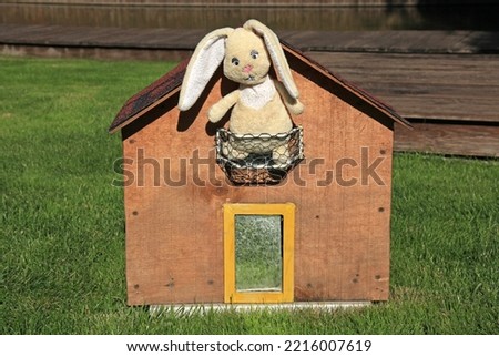 A toy rabbit made of plush sits on the balcony of a small house. Rabbit - a symbol of 2023 year according to the eastern calendar. New Year of 2023. Сhristmas, holidays and celebration concept
