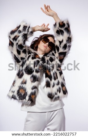 High fashion photo of a beautiful elegant young woman in a pretty leopard print fur coat, stylish sunglasses, trousers, pants posing on white background. Slim figure. Studio shot.
