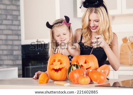 Kid on Halloween party making carved pumpkin with a little help from her mother