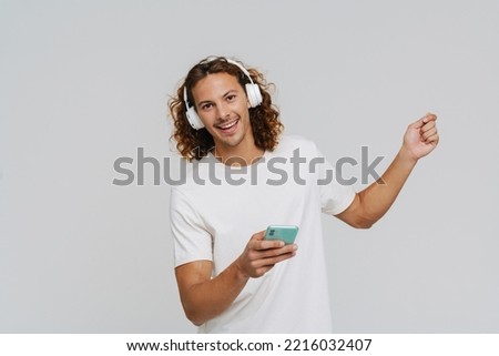 Ginger european man in headphones smiling and using cellphone isolated over white background