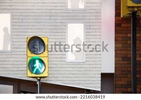 Outside view of the silhouettes of a woman and a man in the windows on the facade of a white brick wall of the house . The burning green signal of the traffic light