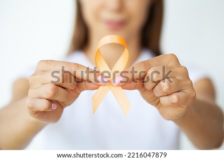 Woman in white t-shirt holding and showing orange awareness ribbon in her hands Royalty-Free Stock Photo #2216047879