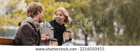 smiling young couple chatting and holding paper cups with coffee to go, banner