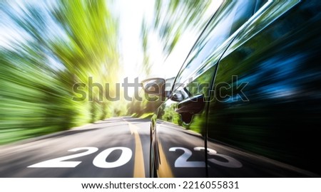 Car in motion blur driving to forest with new year number 2023  and arrow sign on the road