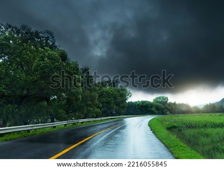 Empty curved wet road against stormy clouds Royalty-Free Stock Photo #2216055845