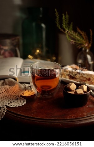 Hugge evening with a cup of tea, a book and dessert. A hot drink on a round wooden table, a book and a piece of homemade cake Royalty-Free Stock Photo #2216056151