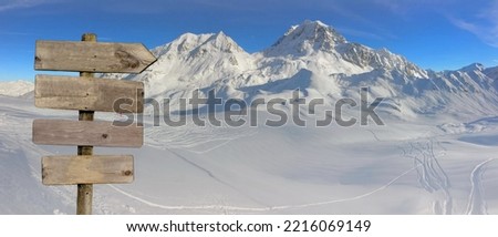 wooden directional post with arrow pointing right on  ski slopes in snow capped  peak mountain background 