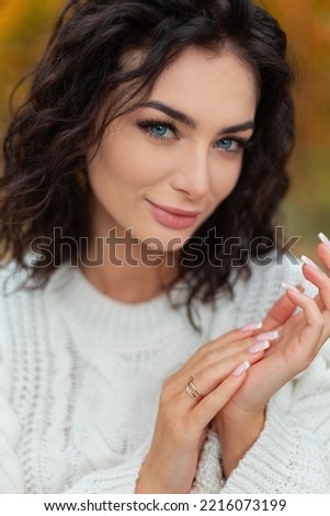 Natural portrait of beautiful young woman with amazing blue eyes in a fashion white knit sweater is rubbing her hands and walking in an autumn bright yellow park with golden leaves.