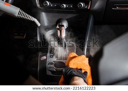 Steam cleaning of gearbox and dashboard in car. Vaping steam. Cleaning individual elements of black leather interior in auto. Creative advert for auto detailing service Royalty-Free Stock Photo #2216122223