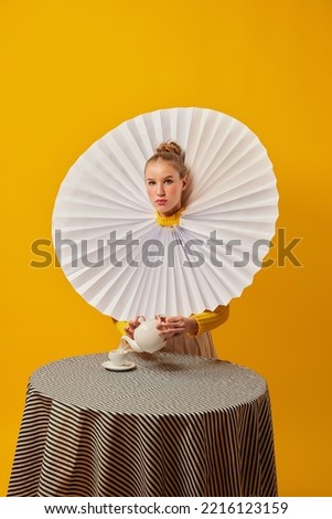 Tea party. Young indifferent girl in giant jabot collar or neckwear and yellow tights isolated over yellow background. Contemporary art. Royalty-Free Stock Photo #2216123159
