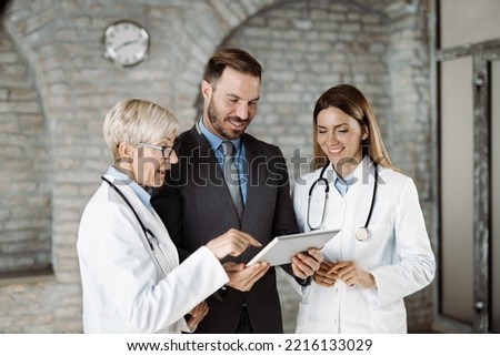Two female doctors and businessman using  touchpad in a hospital.  Focus is on businessman