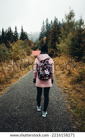 Portrait of young tourist woman with backpack in colorful autumn misty and foggy forest. Female turist during the hike - vertical photo from back.