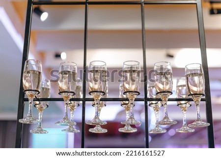 bunch of glasses with champagne standing on rack in restaurant on buffet, blurry lights on background, celebrating party