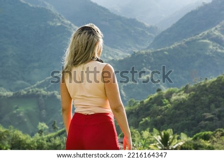 beautiful young caucasian latina woman enjoying a sunset on top of a colombian mountain. girl in summer clothes hiking and admiring the view of the beautiful south american jungle mountains.