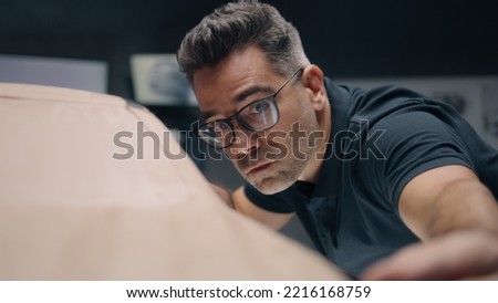 Male middle aged automotive designer working on futuristic car model from plasticine clay. Future design of new generation electric car. Work in modern car design studio. Royalty-Free Stock Photo #2216168759
