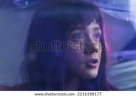 White teenage girl with purple hair looking away from camera with anxious expression behind layer of plastic wrap. Artistic portrait. Horizontal shot. High quality photo
