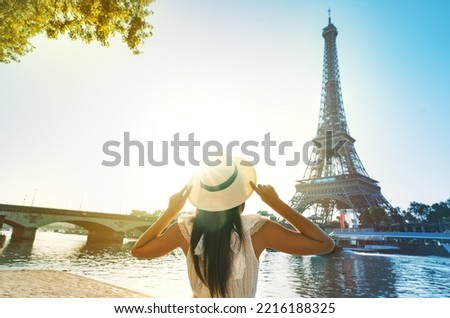 Young woman tourist in sun hat and white dress standing in front of Eiffel Tower in Paris at sunset. Travel in France, tourism concept Royalty-Free Stock Photo #2216188325