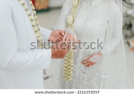 Married couple exchange wedding rings at Indonesian wedding ceremony. Groom put a ring on finger of his lovely wife. The couple exchanges the wedding rings. Just married