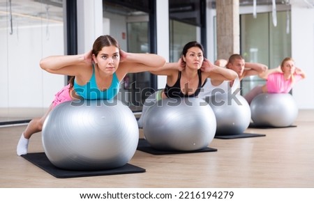 Adult sports people practiciting Pilates in the studio during a group training session perform an exercise on a fitness ball, ..which strengthens the lumbar region and develops overall flexibility Royalty-Free Stock Photo #2216194279