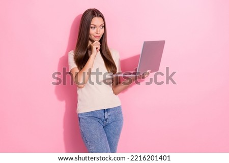 Photo of young nice pretty smart woman wear pastel t-shirt denim jeans hold computer touch chin online education minded isolated on pink color background