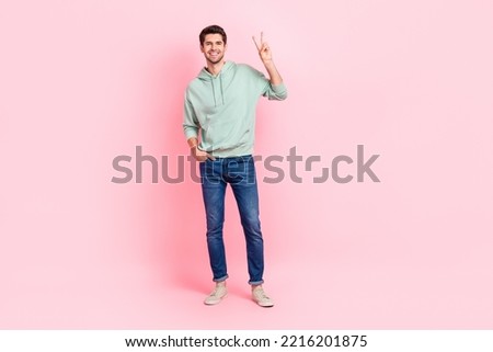 Full length photo of satisfied glad young man put arm pocket demonstrate v-sign isolated on pink color background