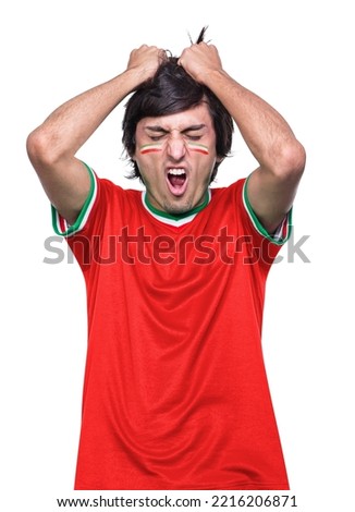 Young sporty soccer fan man with red jersey to IR IRAN, frustrated by the defeat of his favorite team. White background. Royalty-Free Stock Photo #2216206871