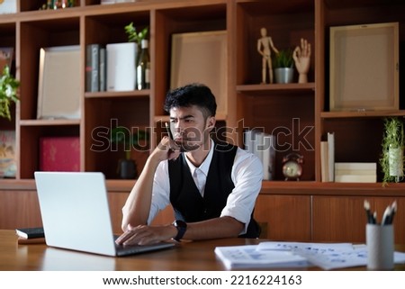 A portrait of a good-looking and discreet Asian man sitting at his desk with a thoughtful look on his computer.