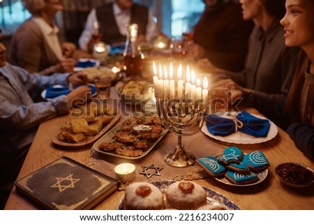 Close up of lit candles in menorah with Jewish multigeneration family celebrating Hanukkah at dining table. Royalty-Free Stock Photo #2216234007