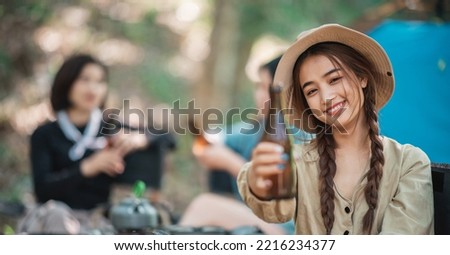 Selective focus young Asian pretty woman and her girlfriend sitting at front of tent, use mobile phone take photo during camping in forest with happiness together