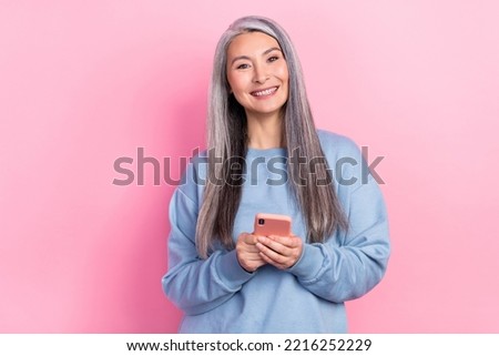 Photo of cute cheerful retired woman blue sweater typing modern device isolated pink color background