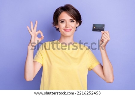 Photo of young attractive nice woman wear yellow t-shirt showing okey sign smile hold new card good offer isolated on purple color background