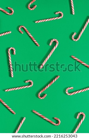 Creative holiday pattern made of red and white striped candy canes on green background. Minimal Christmas spirit aesthetic. New Year flat lay visual.