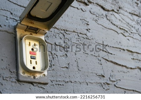 A close up image of an old and damaged outdoor electrical outlet on a grey stucco wall. Royalty-Free Stock Photo #2216256731