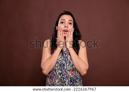 Shocked indian woman with hands on cheeks and open mouth, news hearing, omg sign. Excited lady looking at camera, holding palms on face, amazed person portrait, studio medium shot