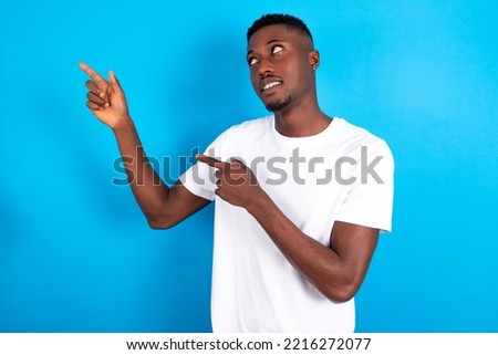 young handsome man wearing white  T-shirt over blue background smile excited directing fingers look empty space