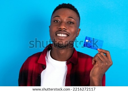 Close up photo of optimistic young handsome man wearing plaid shirt over blue background hold card