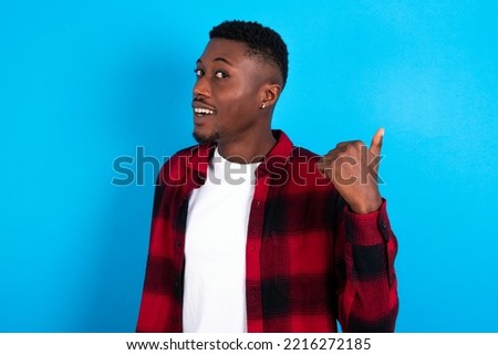 Impressed young handsome man wearing plaid shirt over blue background point back empty space