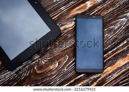 Two black devices, a tablet and a mobile phone lie on a dark wooden textured surface. Royalty-Free Stock Photo #2216279421
