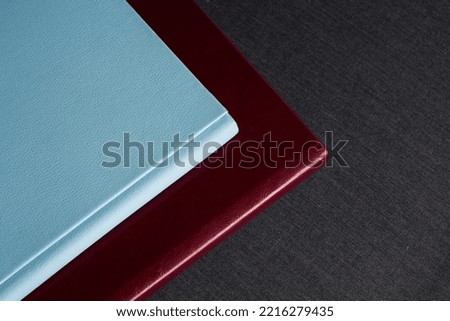 Two stylish photobooks with leather covers, burgundy and blue, of different thicknesses, lie on a dark gray surface in a room.