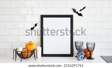 Picture frame mockup with pumpkins, skull, wine glasses, bats on table on brick wall background. Happy Halloween holiday concept.