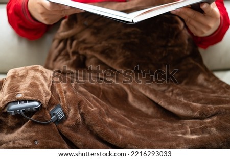 man with an electric blanket and reading a book on a sofa Royalty-Free Stock Photo #2216293033