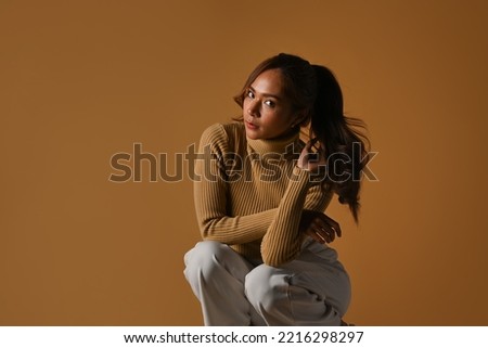 Studio photo of fashionable woman in warm clothes posing on brown background. Autumn and winter fashion concept