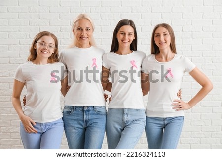 Beautiful women with pink awareness ribbons hugging on white brick background. Breast cancer concept