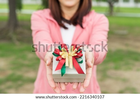 Hands female holding a gift wrapped with ribbon. Shallow depth of field with focus on the box. Hand woman giving a gift box in park for Birthday, Christmas, New year, Valentine's, Graduate, Celebrate.