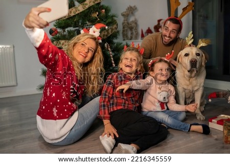 Beautiful blonde mom taking a selfie with her family and their dog. They all have Christmas decorations on their heads