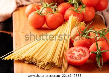 Pasta, beautiful details of red tomatoes and strands of raw spaghetti over rustic wood, selective focus. Royalty-Free Stock Photo #2216347855